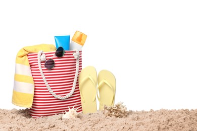 Stylish bag with beach accessories on sand against white background