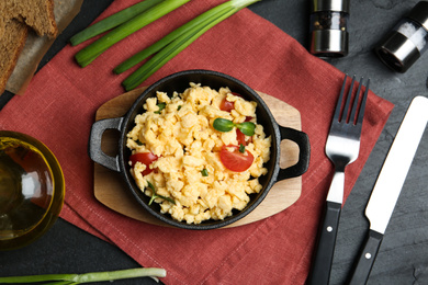 Tasty scrambled eggs served on black table, flat lay