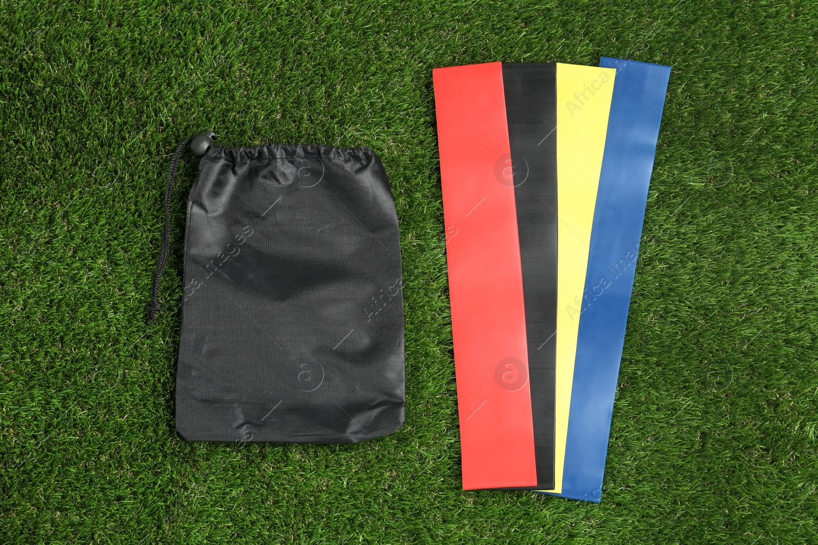 Photo of Fitness elastic bands and bag on green grass, flat lay