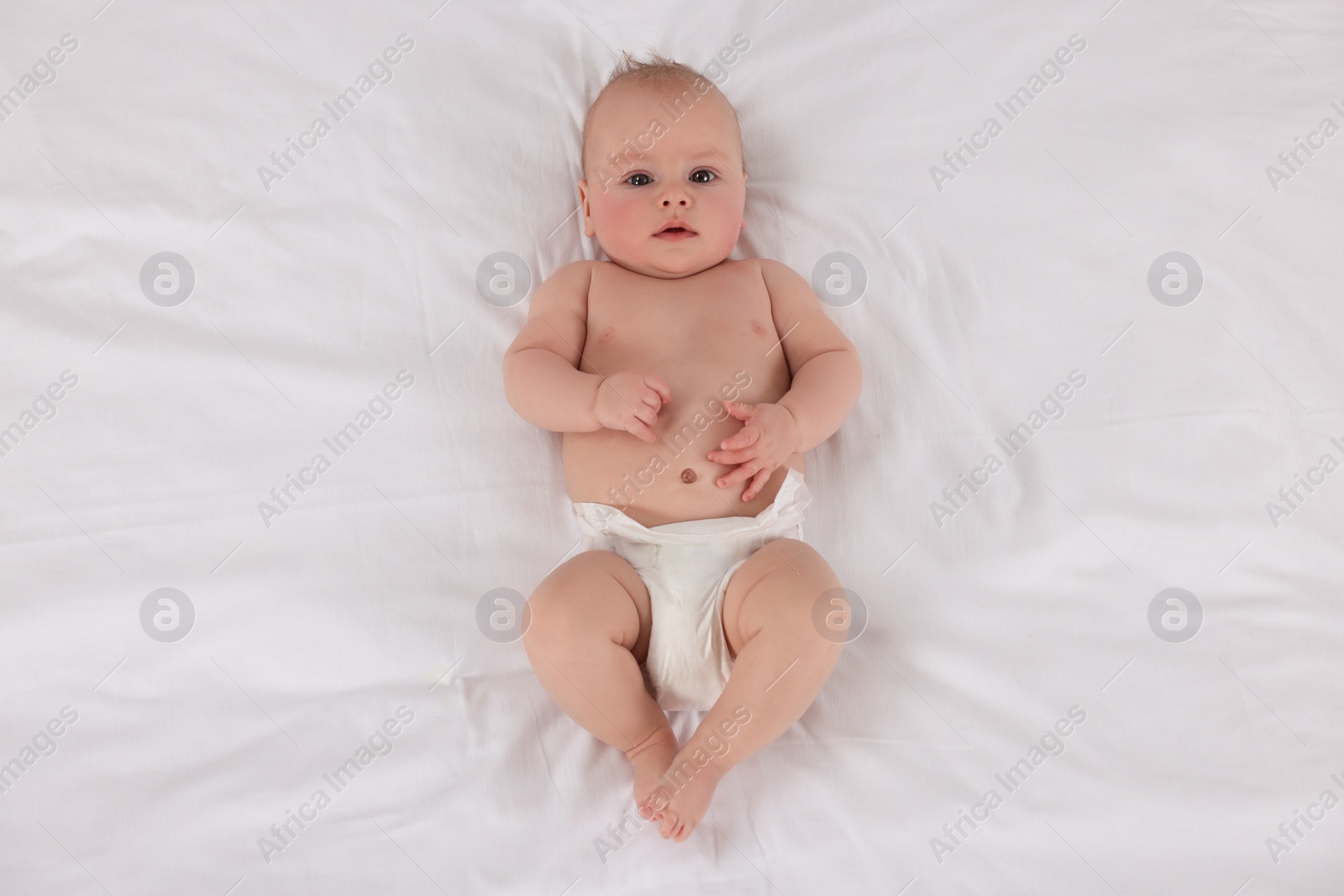 Photo of Cute little baby in diaper lying on bed, top view