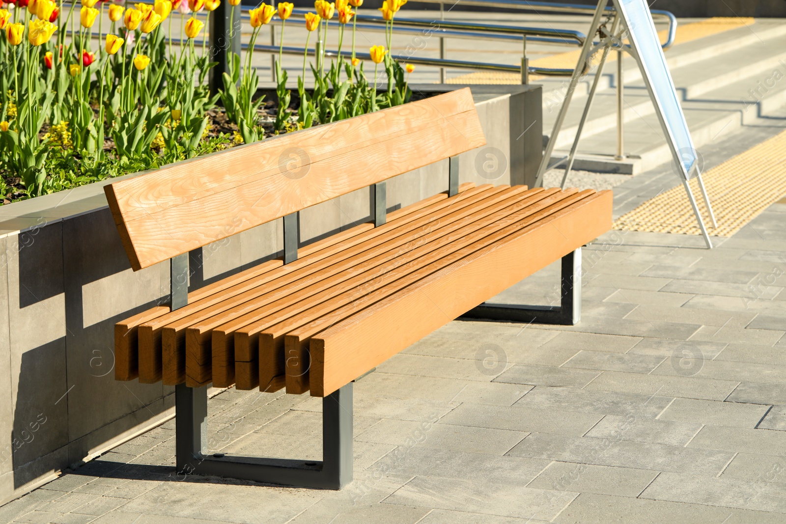 Photo of Wooden bench near flowerbed outdoors on sunny morning