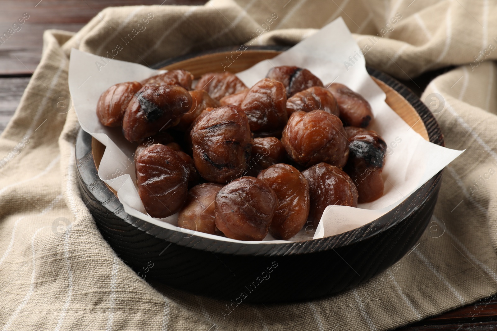 Photo of Roasted edible sweet chestnuts in bowl on table, closeup