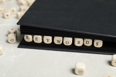 Beads with word KEYWORDS in notebook on light marble table, closeup