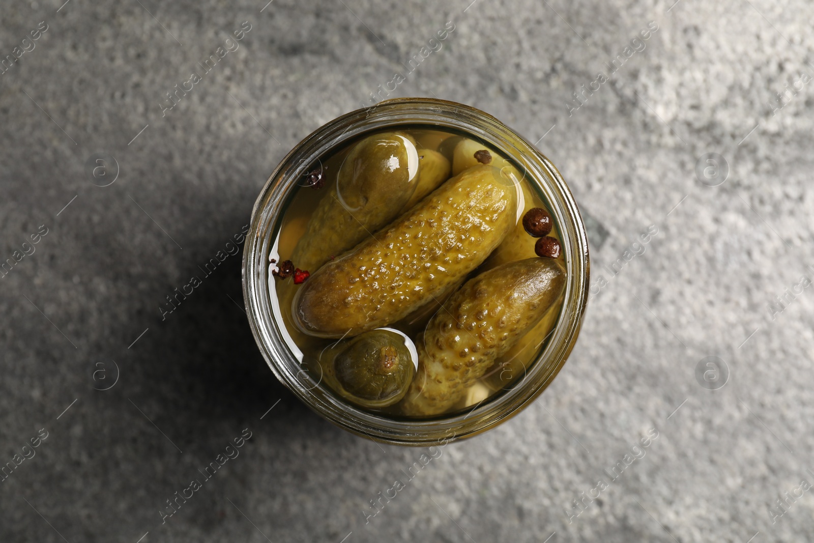 Photo of Tasty pickled cucumbers in glass jar on grey table, top view