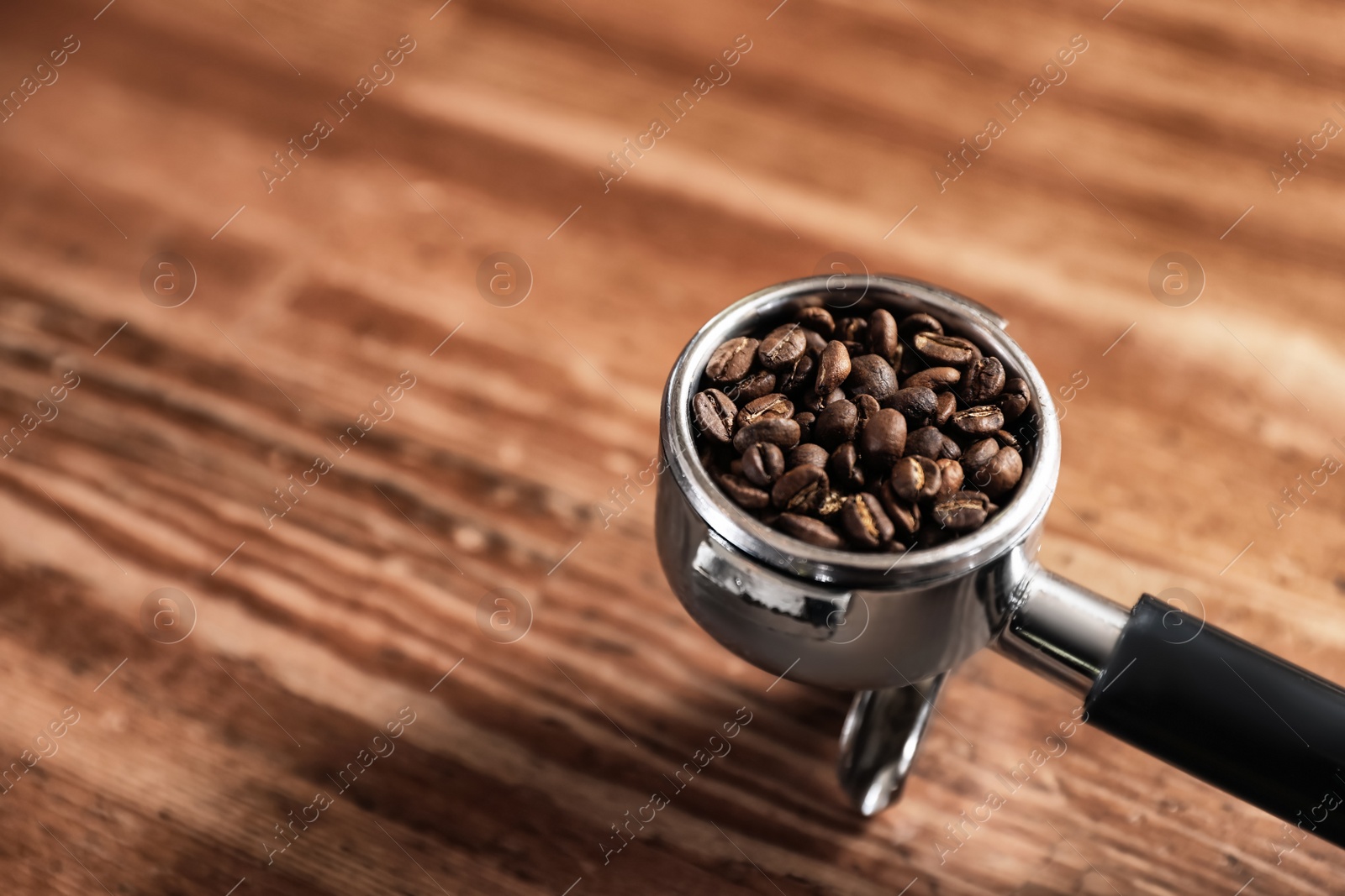 Photo of Portafilter with roasted coffee beans on wooden table. Space for text