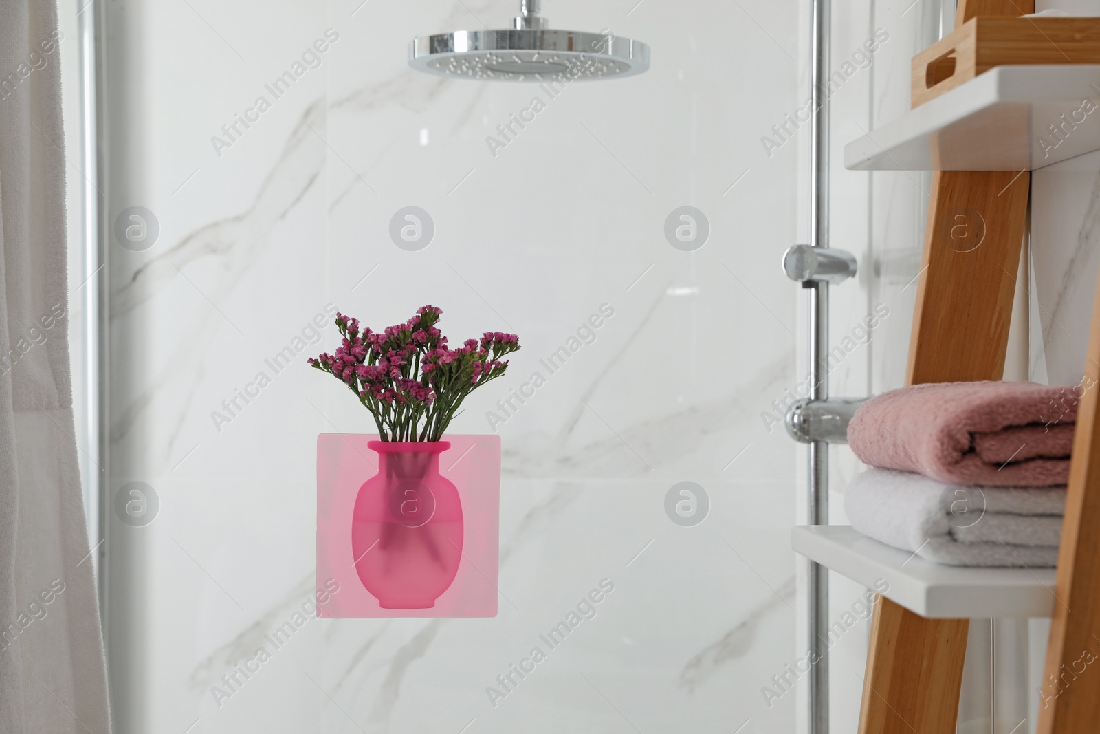 Photo of Silicone vase with flowers on shower glass panel in stylish bathroom