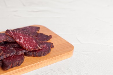 Photo of Pieces of delicious beef jerky on white textured table, closeup. Space for text