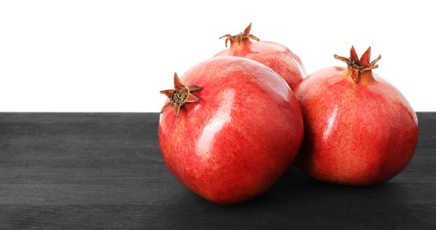 Fresh pomegranates on black wooden table against white background, space for text