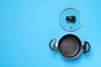 Photo of Empty pot and glass lid on light blue background, flat lay. Space for text