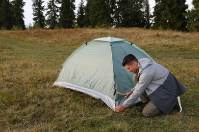 Man setting up grey camping tent outdoors