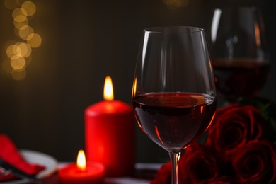 Photo of Glasses of red wine, burning candles and rose flowers against blurred lights, space for text. Romantic atmosphere