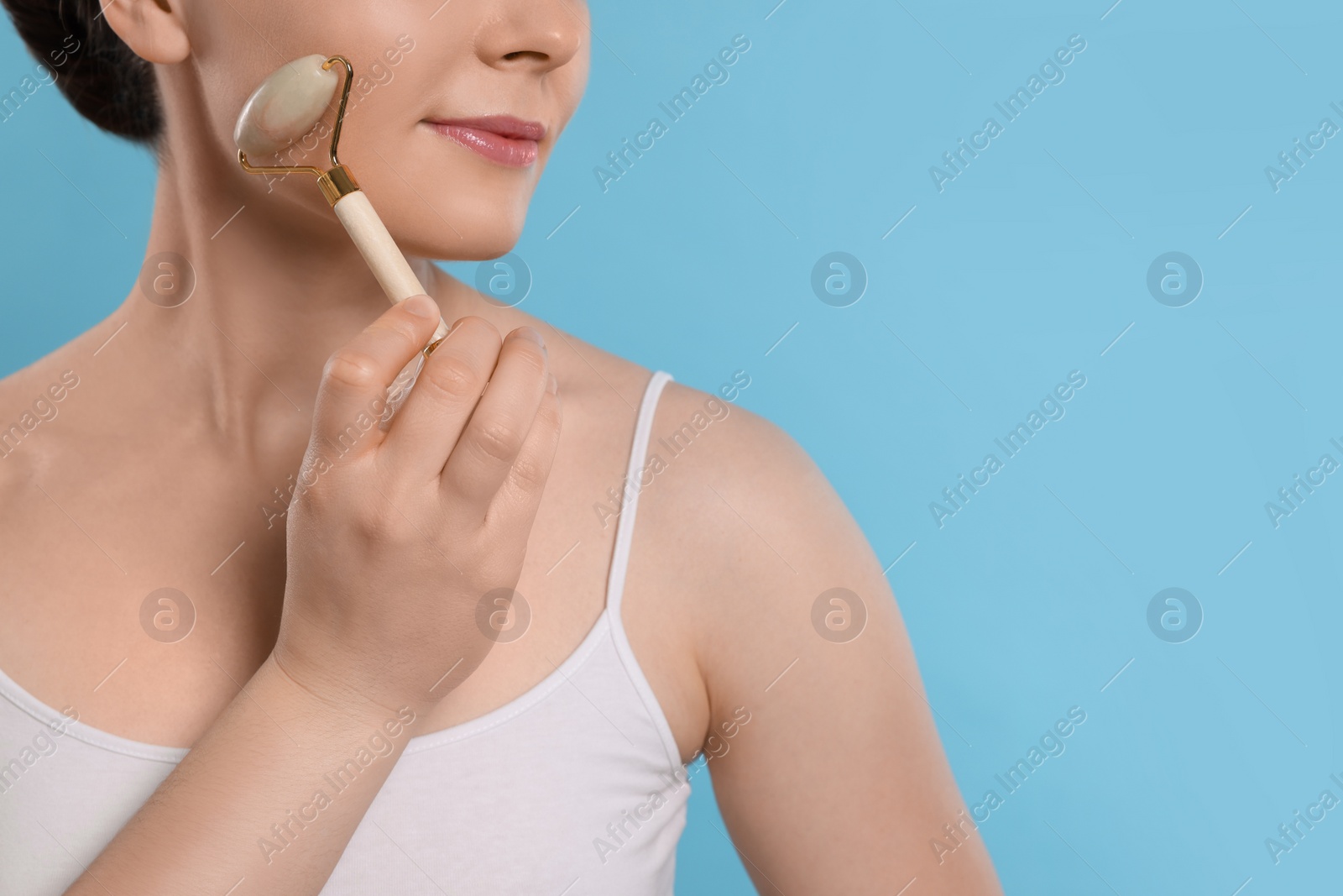 Photo of Young woman massaging her face with jade roller on turquoise background, closeup. Space for text