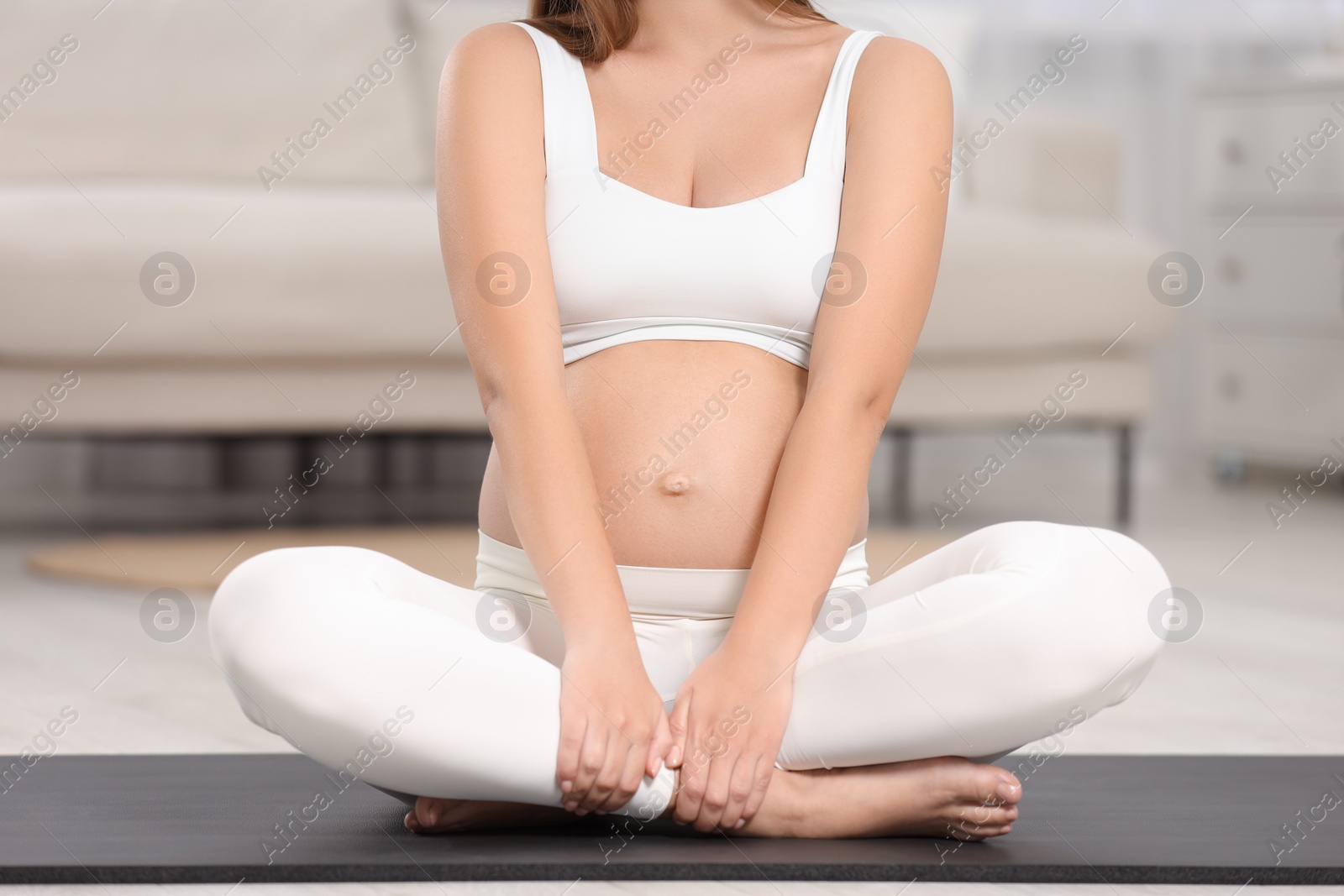 Photo of Pregnant woman doing exercises on yoga mat at home, closeup