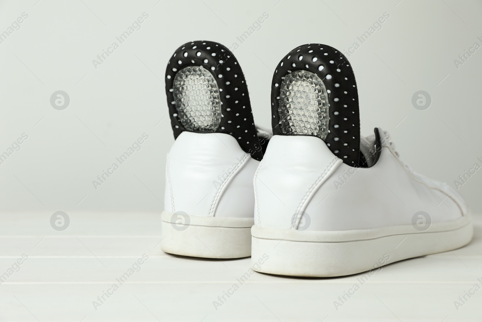 Photo of Orthopedic insoles in shoes on white wooden floor, closeup. Space for text