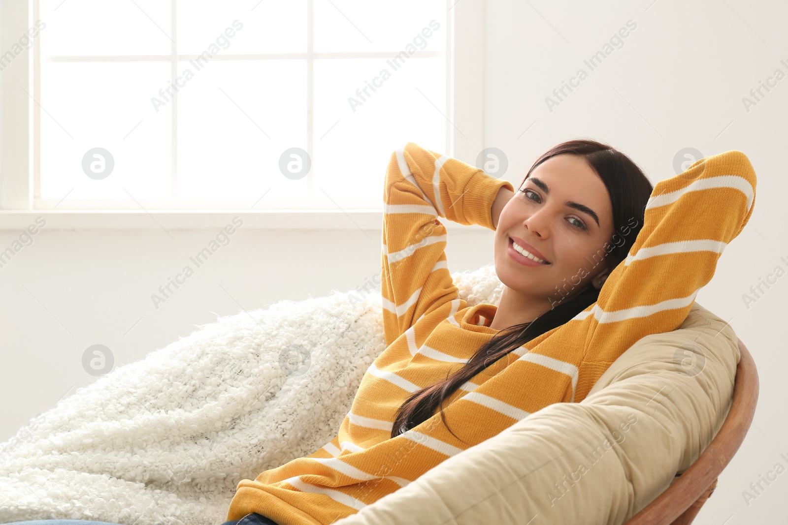 Photo of Young woman relaxing in papasan chair near window at home