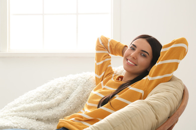 Photo of Young woman relaxing in papasan chair near window at home