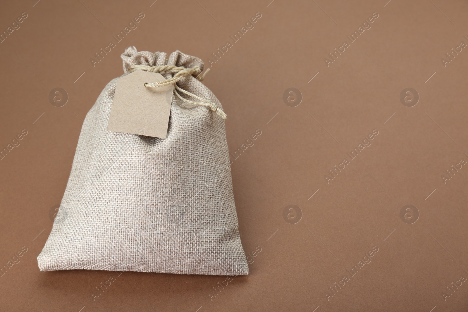 Photo of Tied burlap bag with tag on brown background. Space for text