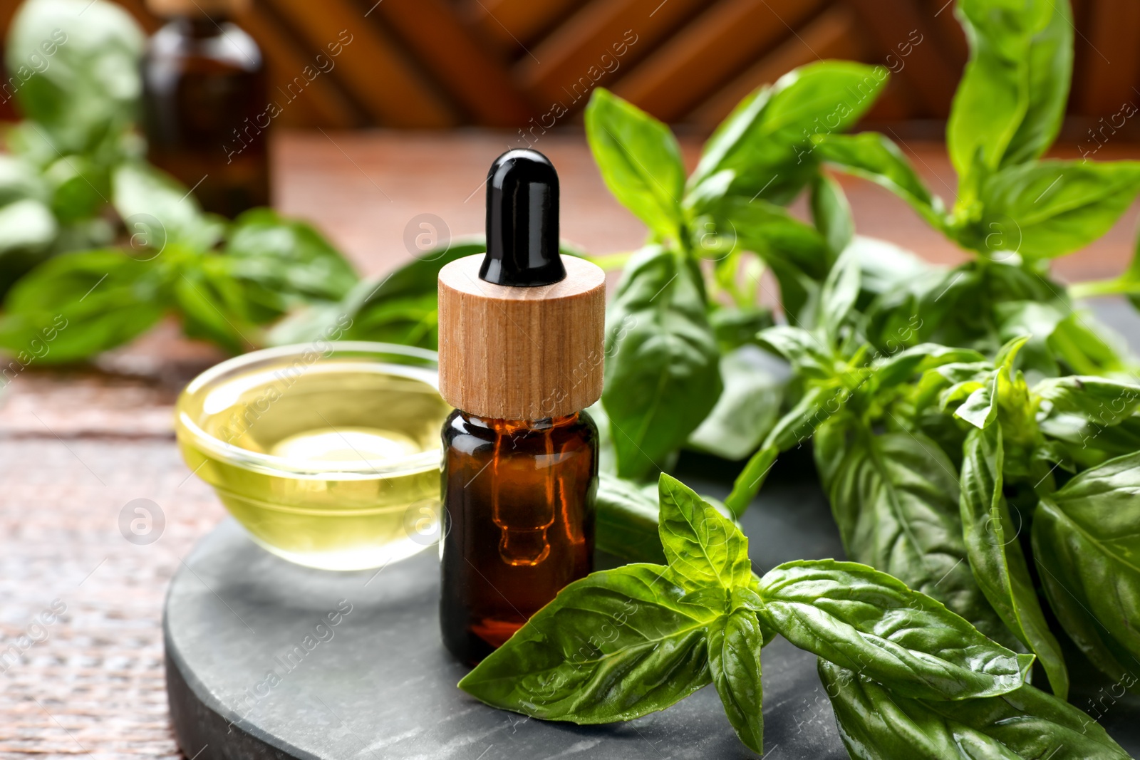 Photo of Basil essential oil and fresh leaves on wooden table, closeup