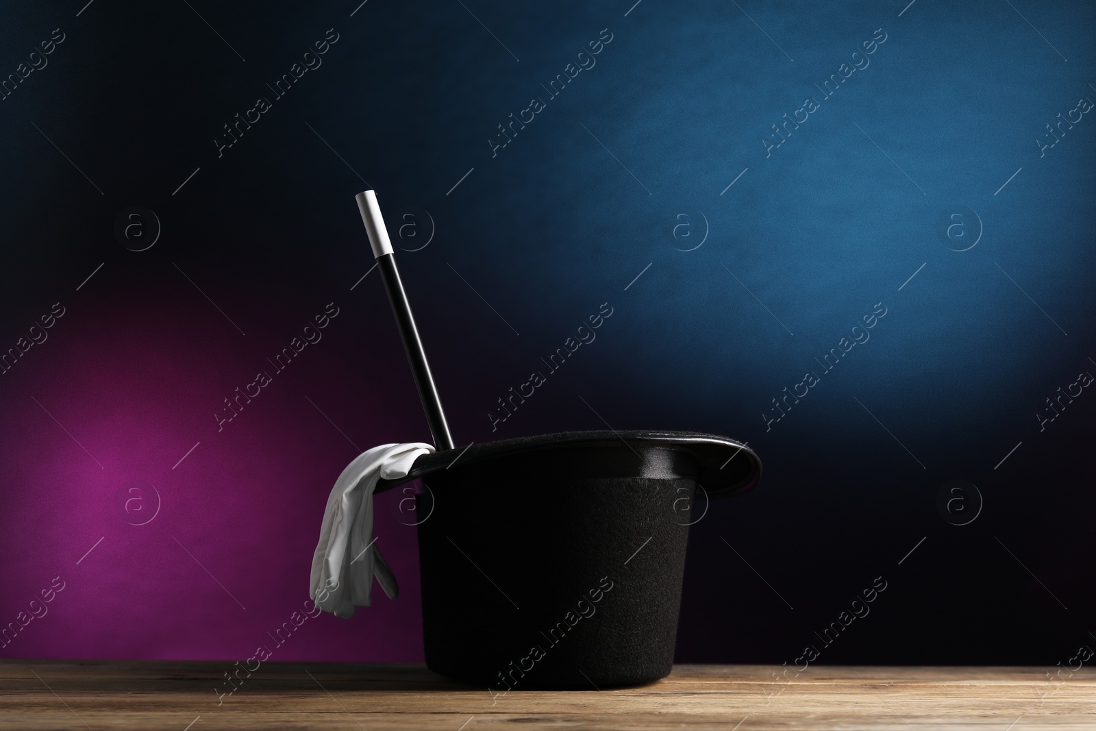 Photo of Magician's hat, gloves and wand on wooden table against dark background