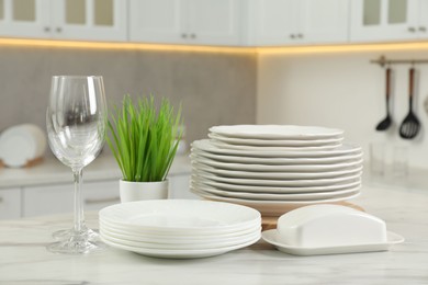 Clean plates, glasses, butter dish and floral decor on white marble table in kitchen