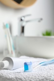 Photo of Plastic toothbrush with paste and tube on white towel in bathroom, closeup. Space for text