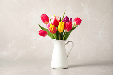 Photo of Beautiful spring tulips in vase on table against light marble background