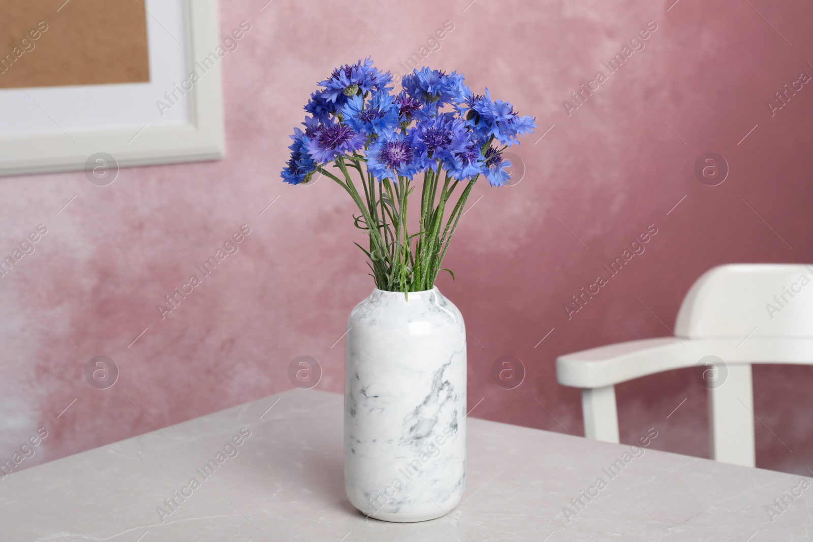 Photo of Bouquet of beautiful cornflowers in vase on light table at home.