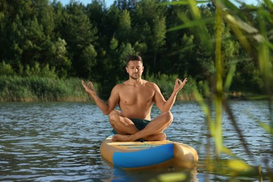 Man meditating on color SUP board on river