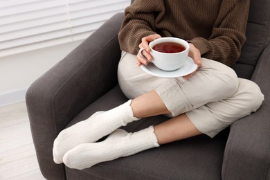 Photo of Woman in warm socks relaxing with cup of tea at home, closeup. Space for text