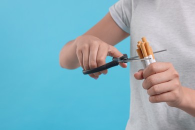 Stop smoking concept. Woman cutting cigarettes on light blue background, closeup. Space for text