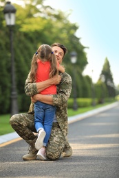 Father in military uniform hugging his little daughter at sunny park