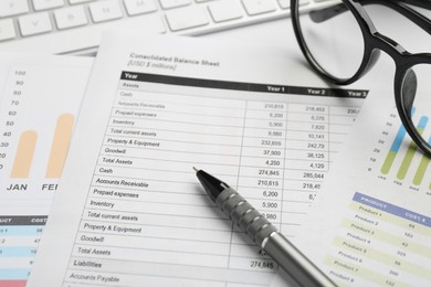 Photo of Accounting documents, pen, glasses and computer keyboard on white table, closeup