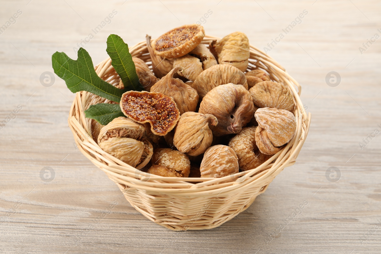 Photo of Wicker basket with tasty dried figs and green leaf on light wooden table