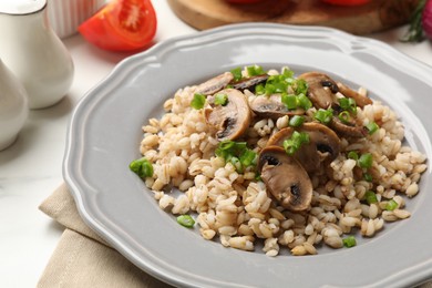 Photo of Delicious pearl barley with onion and mushrooms on white table, closeup