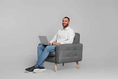 Photo of Smiling young man working with laptop in armchair on grey background