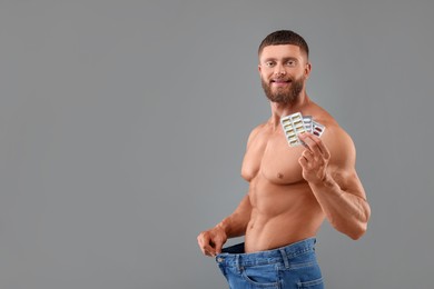 Photo of Athletic young man with pills wearing big jeans on grey background, space for text. Weight loss