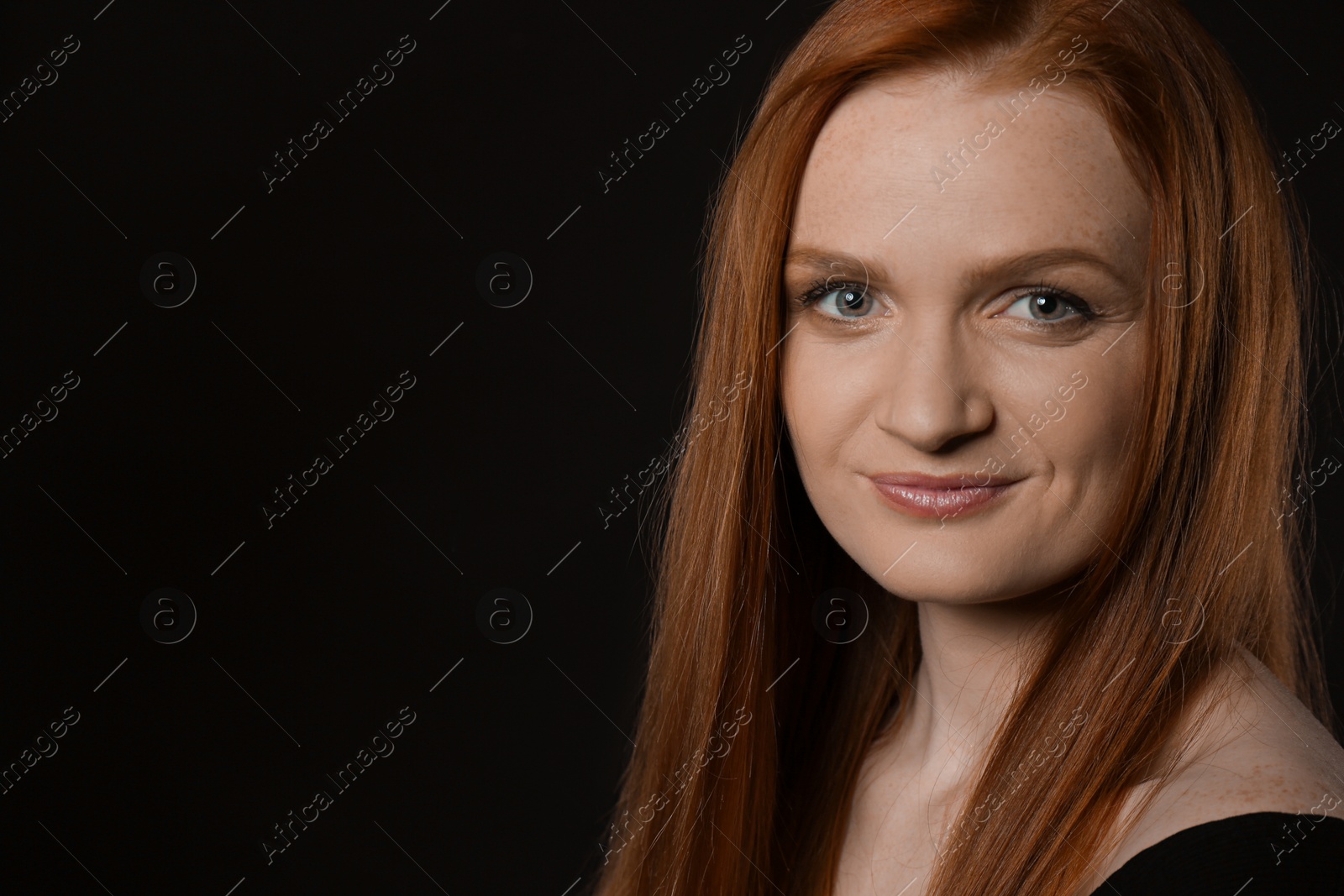 Photo of Candid portrait of happy young woman with charming smile and gorgeous red hair on dark background, space for text