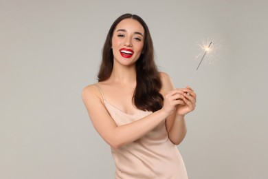 Photo of Christmas celebration. Beautiful young woman with sparkler on grey background