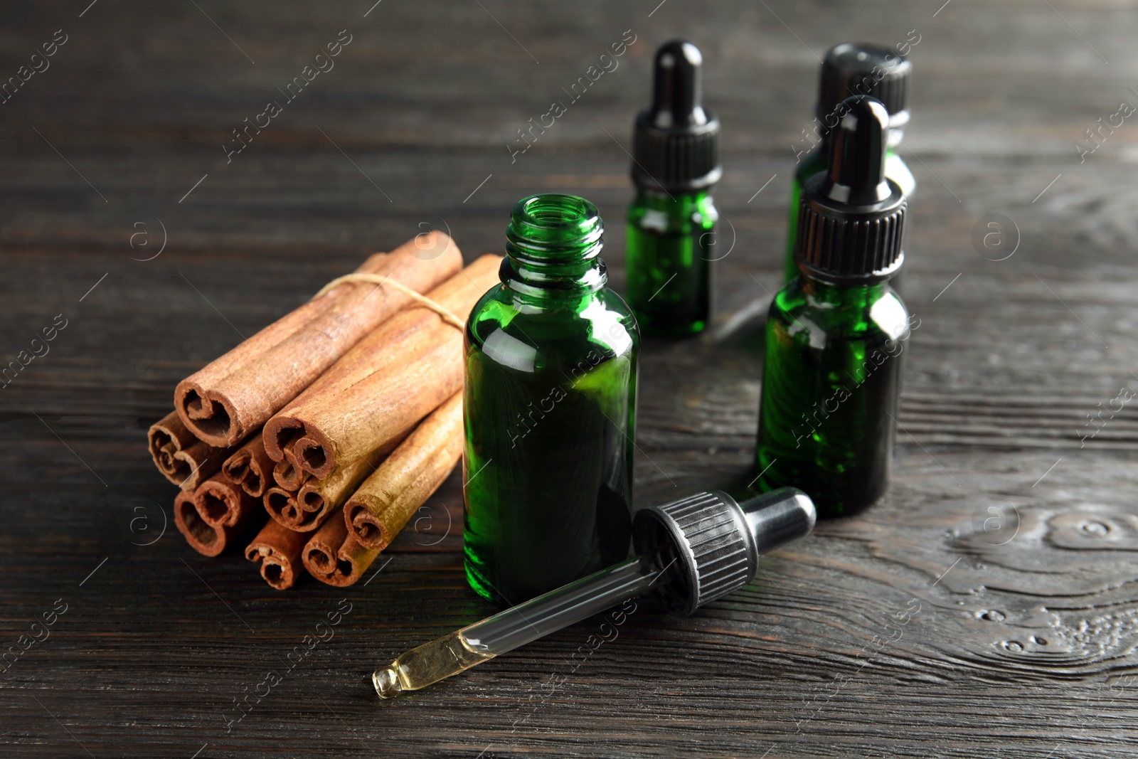 Photo of Bottles with essential oil and cinnamon sticks on black wooden table