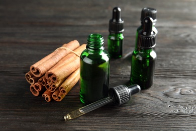 Photo of Bottles with essential oil and cinnamon sticks on black wooden table