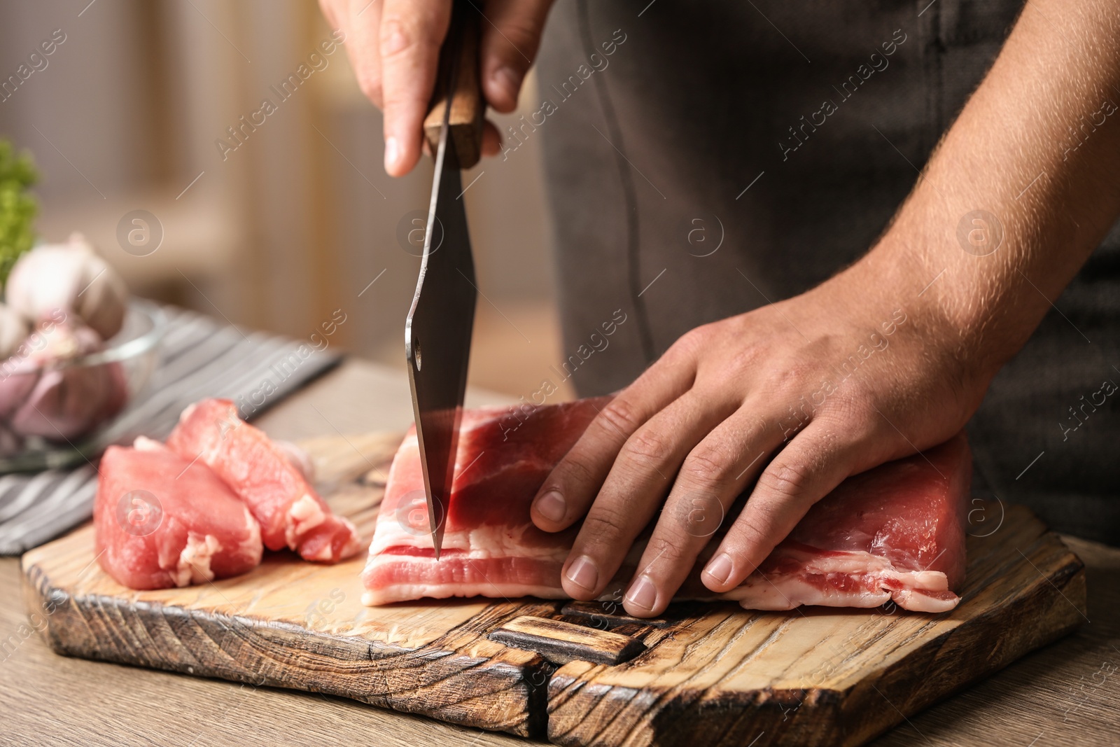 Photo of Man cutting fresh raw meat on table in kitchen, closeup