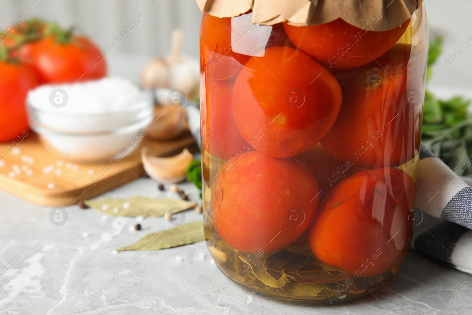 Photo of Pickled tomatoes in glass jar and products on grey table, closeup view