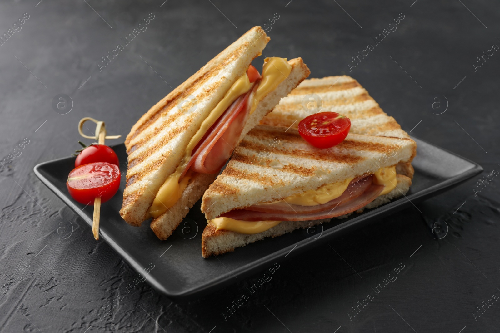 Photo of Tasty sandwiches with ham, melted cheese and tomatoes on black textured table, closeup