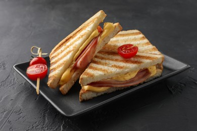 Tasty sandwiches with ham, melted cheese and tomatoes on black textured table, closeup