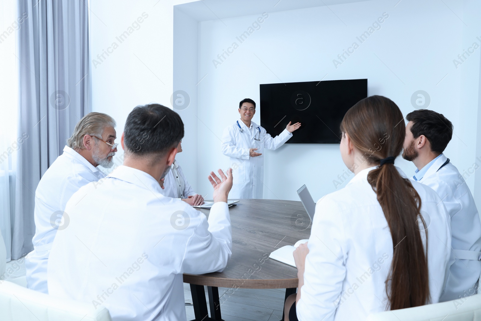 Photo of Team of doctors listening to speaker report near tv screen in meeting room. Medical conference