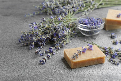 Hand made soap bar with lavender flowers on grey stone table, space for text