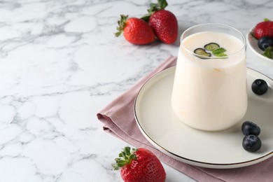 Tasty yogurt in glass and berries on white marble table, closeup. Space for text