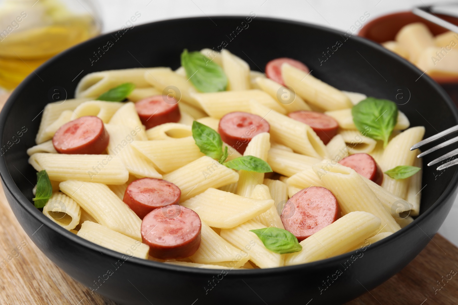 Photo of Tasty pasta with smoked sausage and basil in bowl on table, closeup