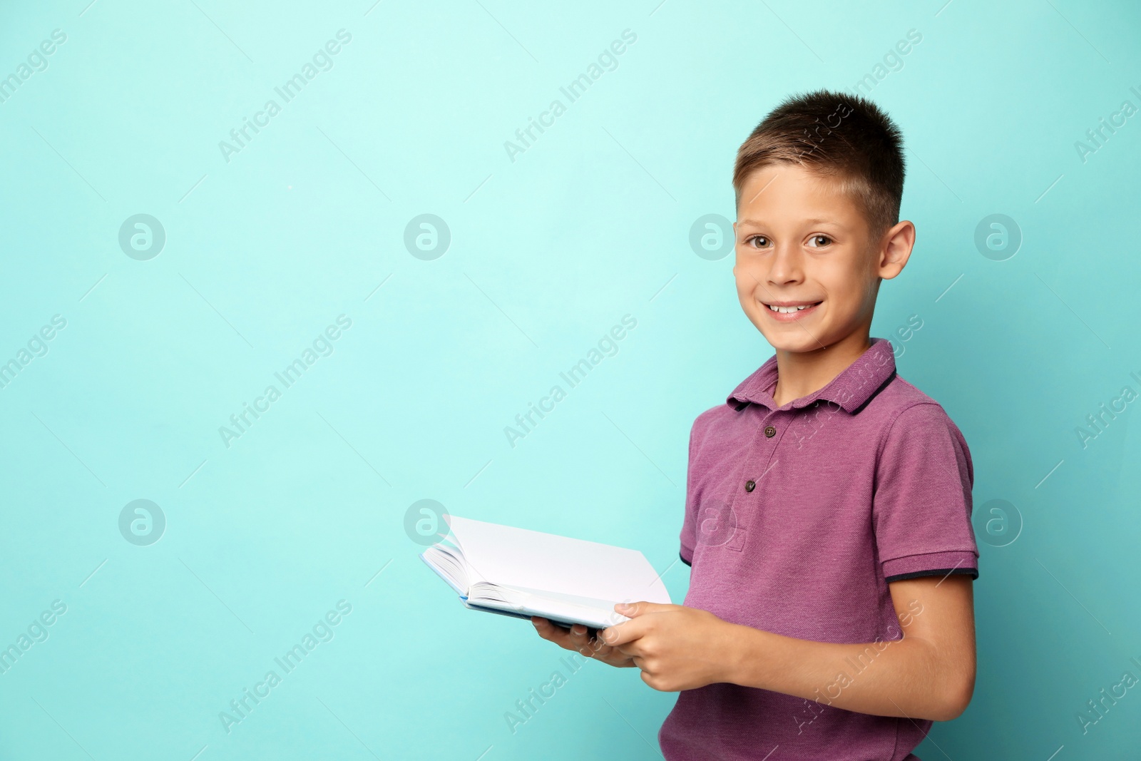 Photo of Portrait of cute little boy reading book on turquoise background. Space for text