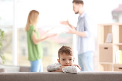 Photo of Little unhappy boy sitting on sofa while parents arguing at home